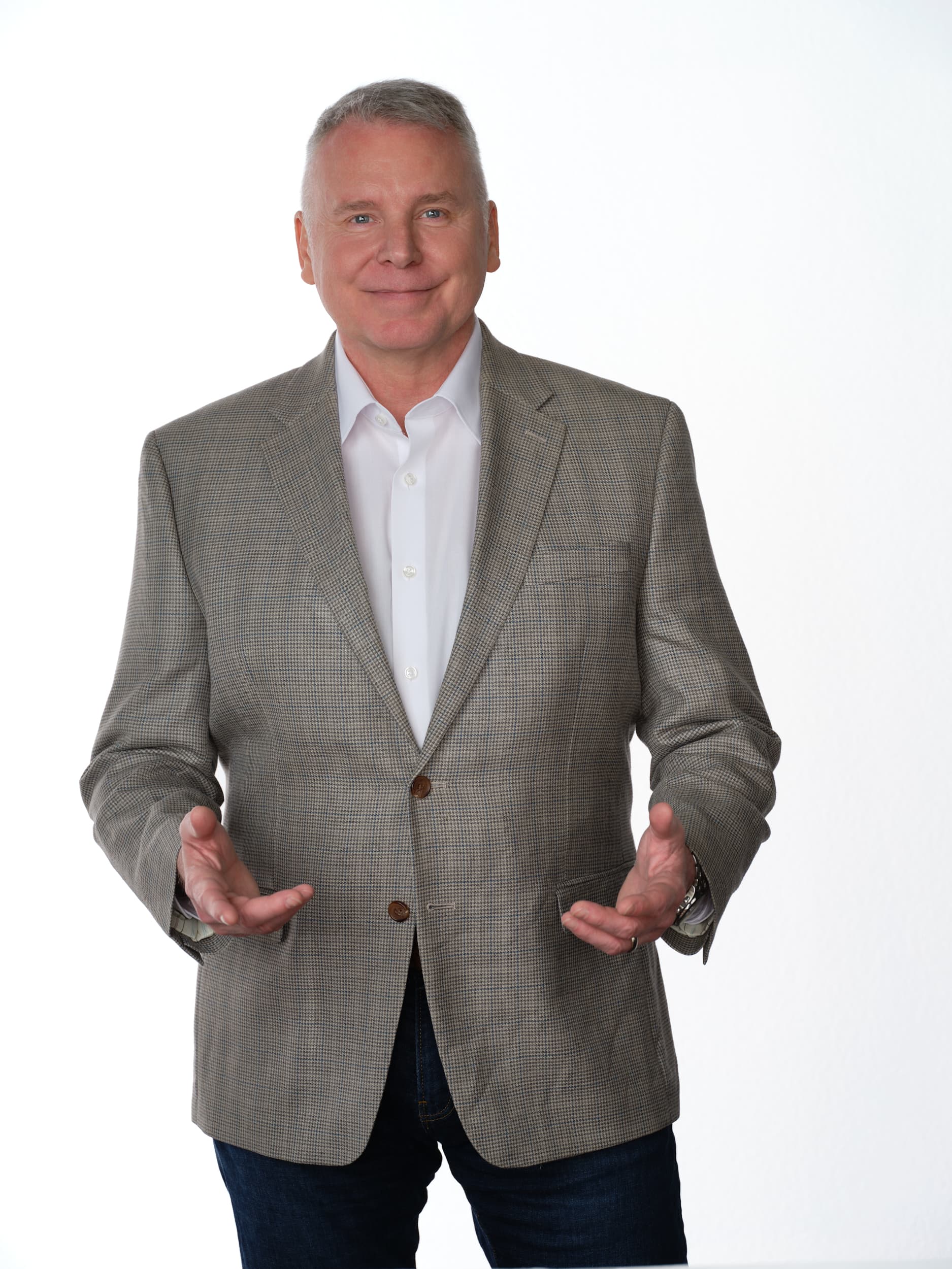Smiling man in a patterned tan blazer and white shirt gesturing with open hands.